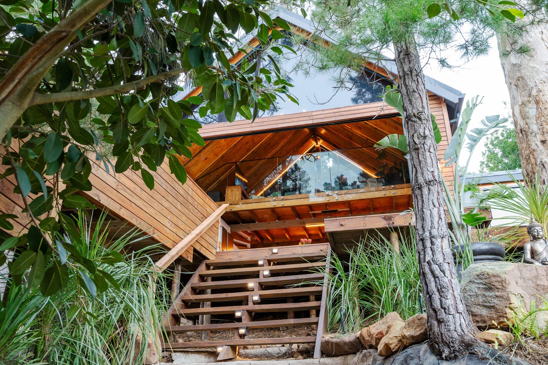 The A-frame from below its lit staircase, warm light under the deck