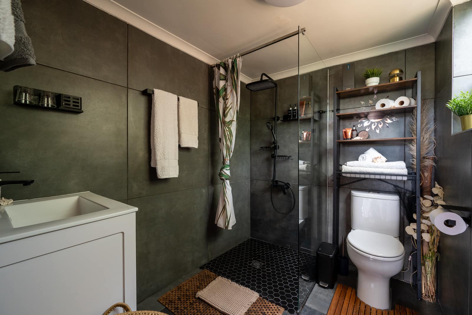 The charcoal bathroom — sage vanity, black rain shower behind glass and warm towels on the rail