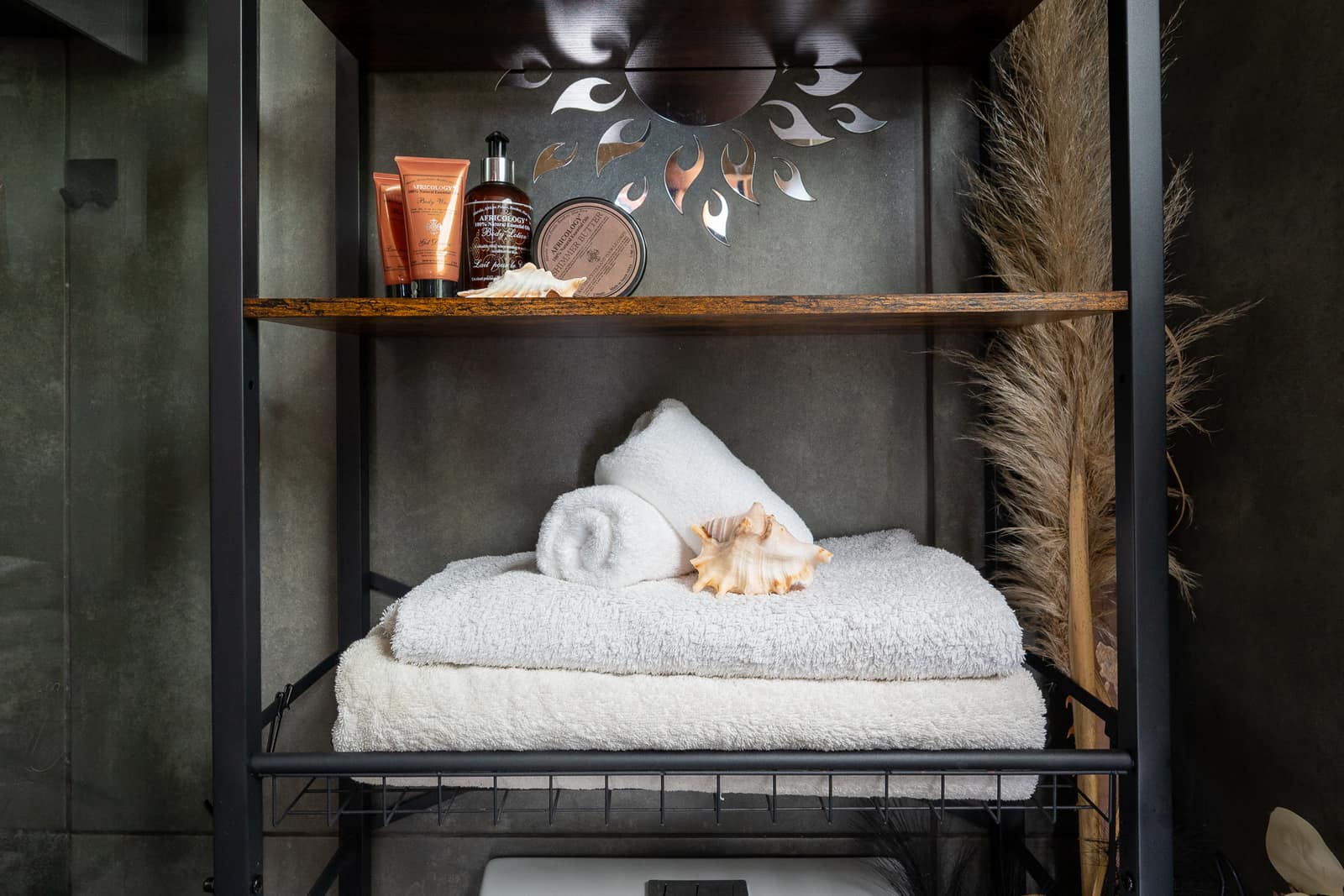Africology amenities and a conch shell on the timber shelf, towels folded below