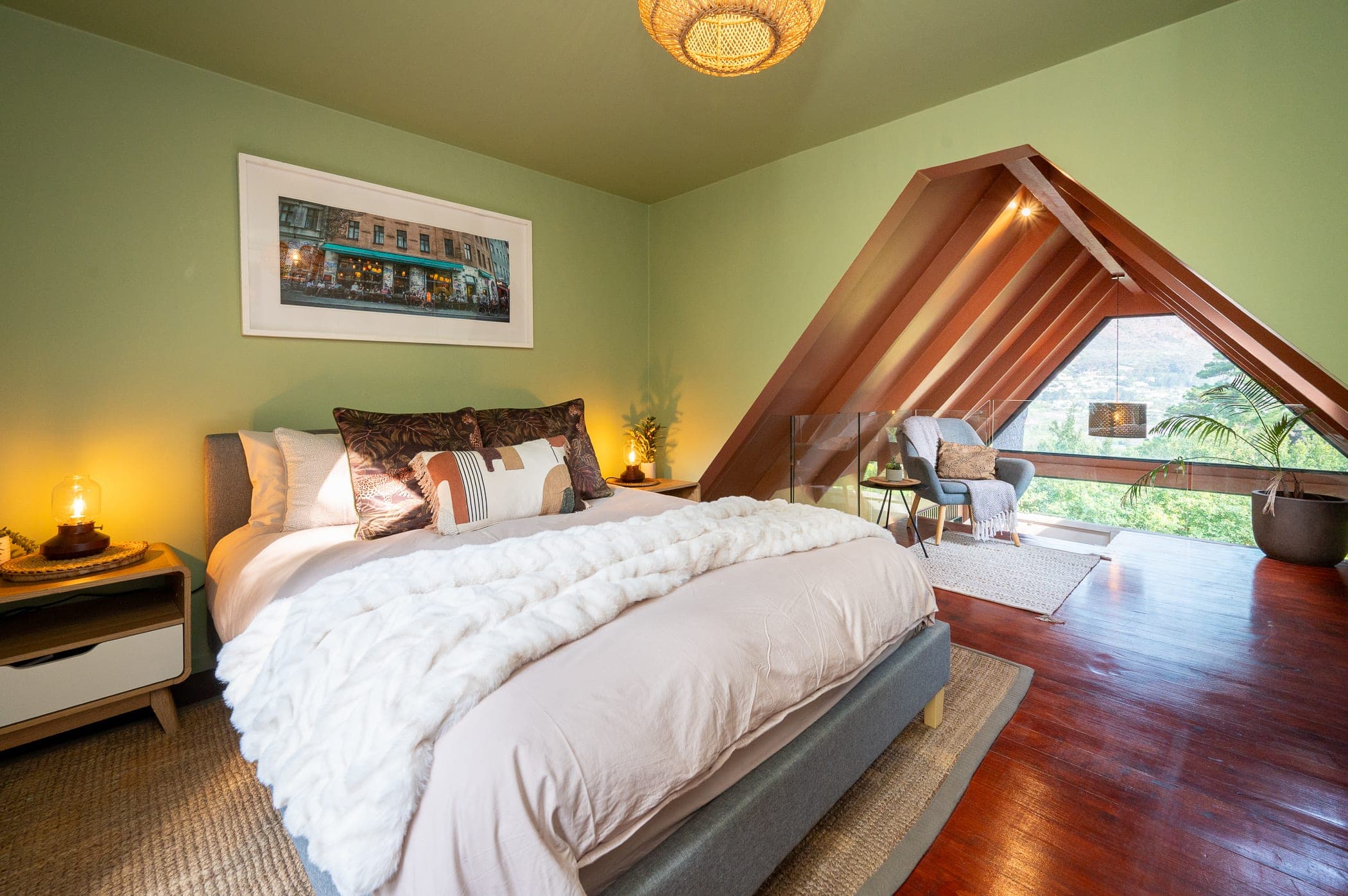 A sage green bedroom opening through the A-frame to the loft nook beyond