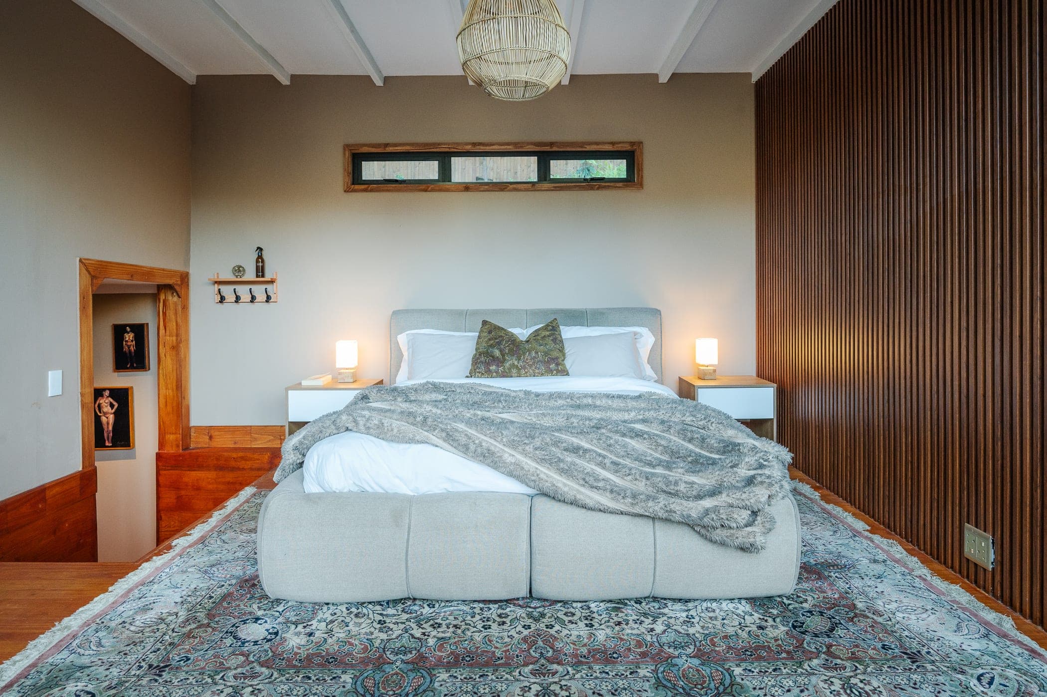 The bed against a slatted timber wall, twin lamps lit and a Persian rug underfoot