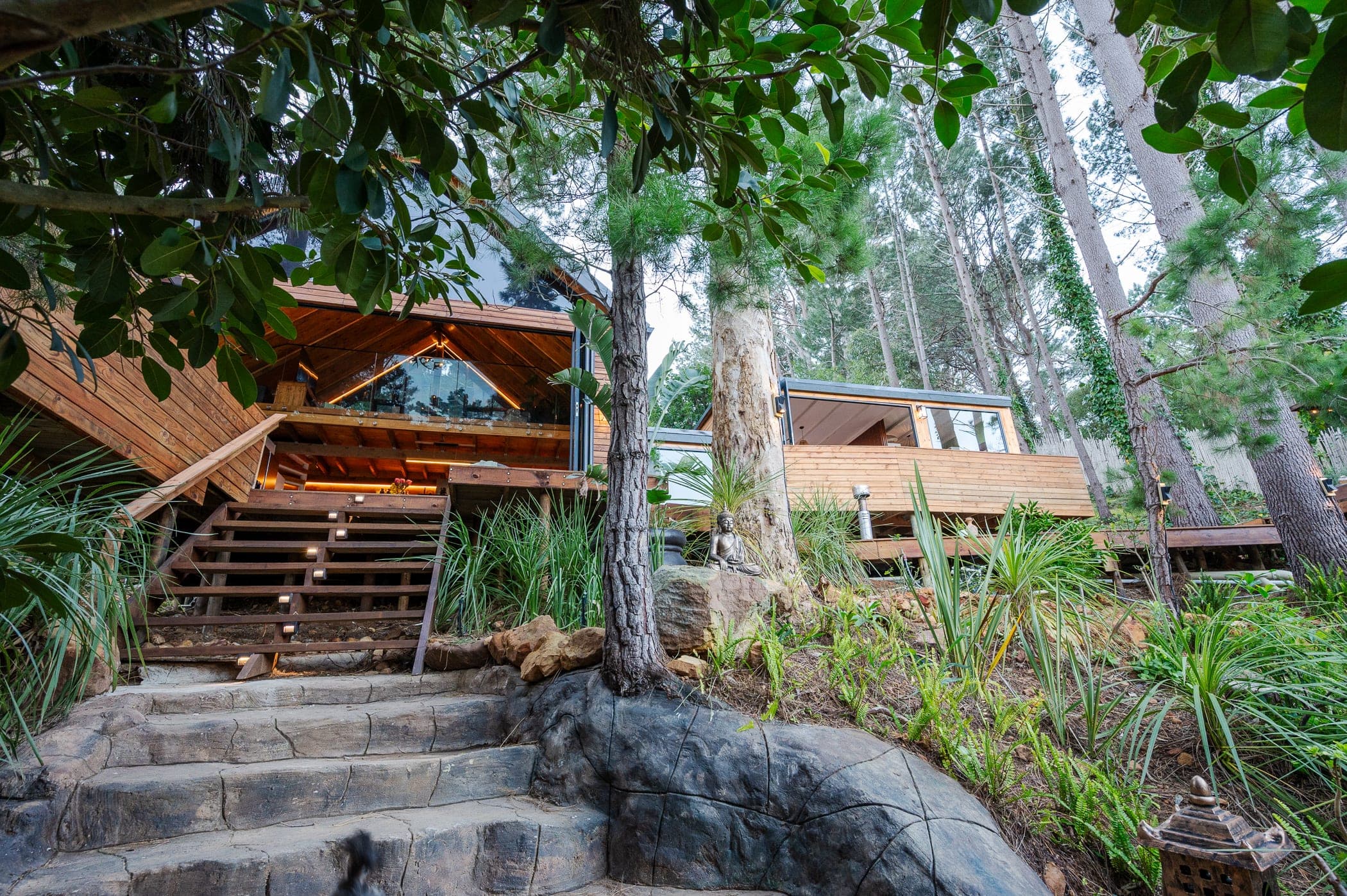 The cabin seen from the garden path at dusk, ferns and a Buddha on the rock
