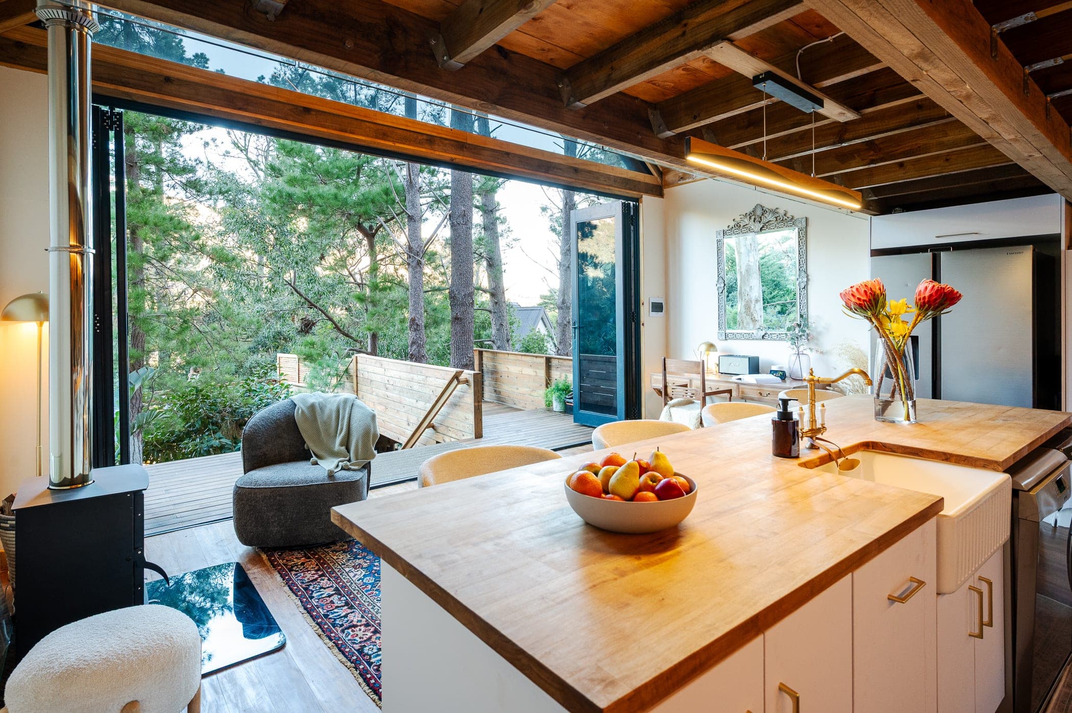 The kitchen island with the whole wall folded open onto the deck and forest
