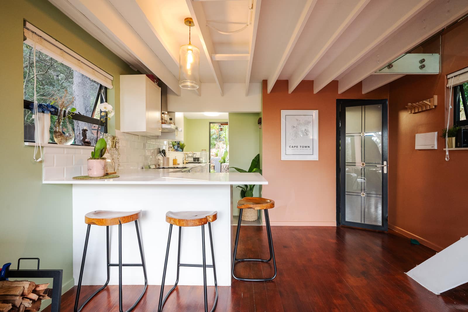Live-edge stools at the white breakfast peninsula, sage and terracotta walls under the beamed ceiling