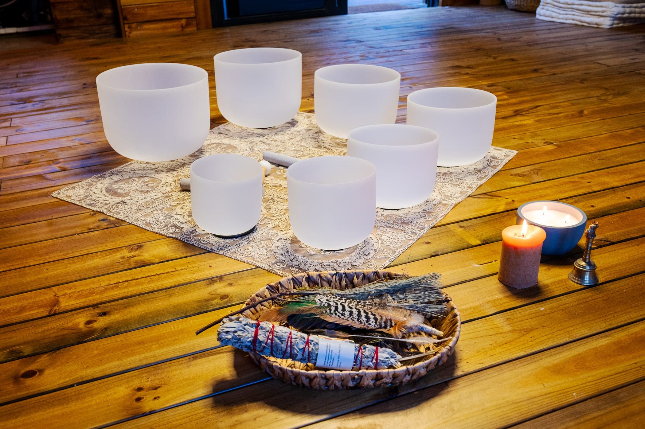 Seven crystal singing bowls on lace, with candles, a brass bell and a tray of feathers and sage