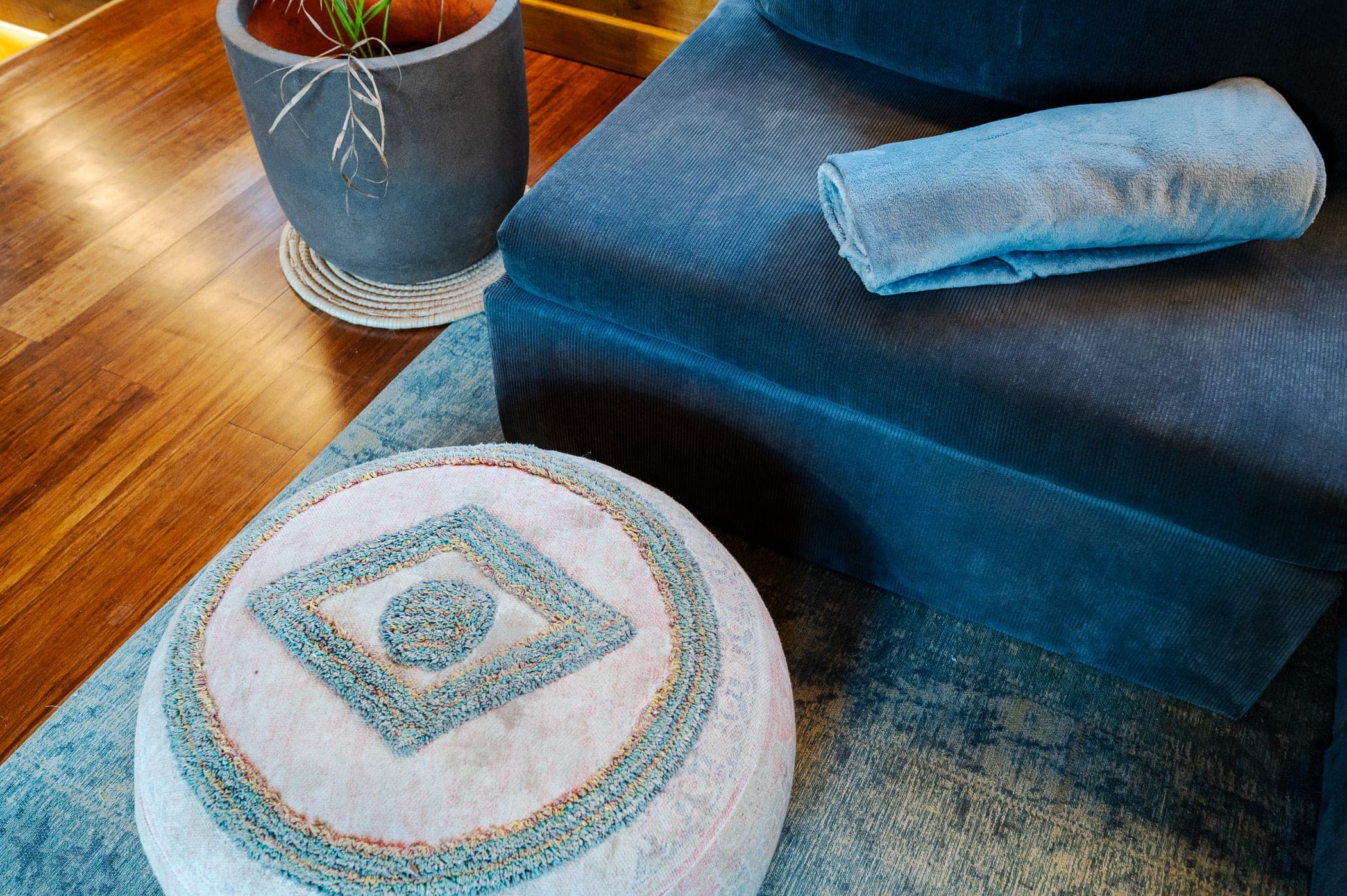 A rolled towel and embroidered pouffe beside the sofa on timber floors