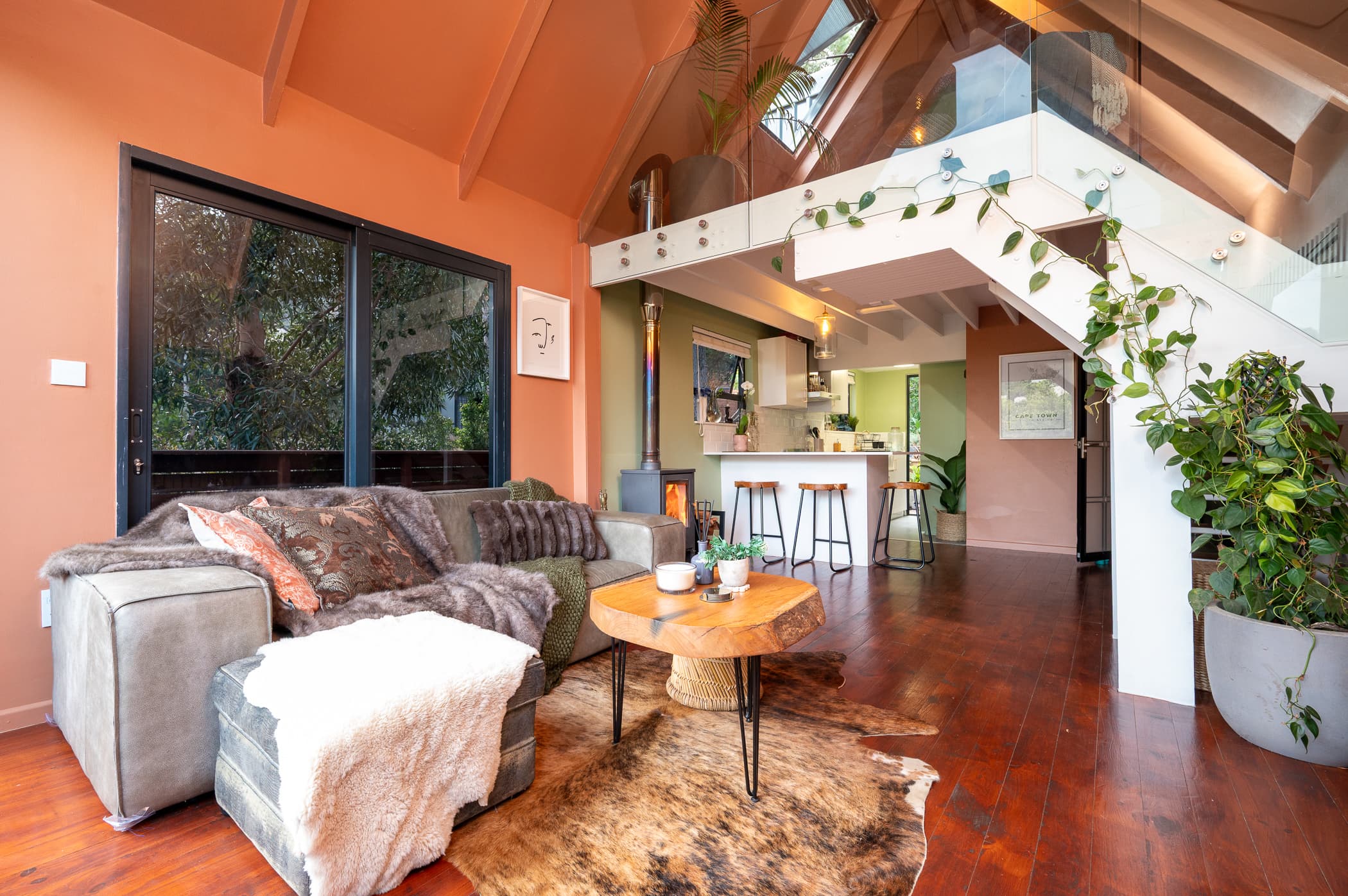 The open-plan living room with a wood-burning stove, deep sofa and the kitchen beneath the mezzanine